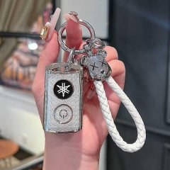 A hand holds a sleek yamaha nmax155 key cover with a snap closure, featuring a silver design and a white braided lanyard. the...