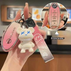 A hand holds a pink nissan key cover with a cute bear charm, showcasing the front view of the key fob buttons for models like...
