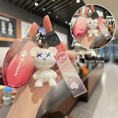 A hand holds a gac trumpchi e8 key cover in pink, featuring a cute bear charm with blue x eyes and a matching strap. the fron...