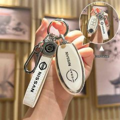 A hand holds a nissan key fob encased in a white leather cover with the nissan logo, featuring a carabiner and a matching key...