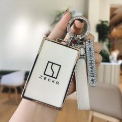 A hand holds a zeekr 001 card key cover, featuring a sleek white design with a silver border and the zeekr logo. the keychain...