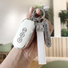 A hand holds a sleek white aito m5 2022 key cover, featuring a diamond-encrusted keychain and numbered charm, designed for mo...