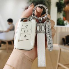 A hand holds a white vw passat 2022 key cover, featuring a premium leather strap and a diamond-encrusted keychain with a numb...
