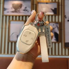 A hand holds a gac gs8 key cover with a sleek, metallic finish and a decorative keychain featuring a numbered charm and leath...
