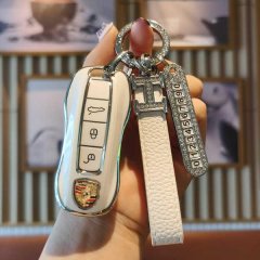 A hand holds a sleek white porsche key cover with a leather strap and numbered charm, designed for panamera, cayenne, macan, ...