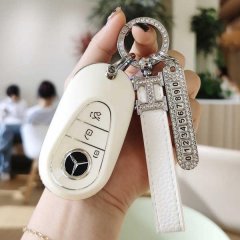 A hand holds a mercedes c260l key fob with a white leather cover, featuring a diamond-encrusted keychain and numbered charm, ...