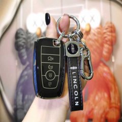 A hand holds a sleek black lincoln key cover, featuring the brand logo and a matching leather strap, designed for models like...
