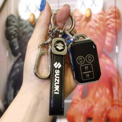 A hand holds a suzuki jimny key cover, featuring a sleek black leather design with a metallic suzuki logo and functional keyc...