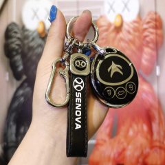 A hand holds a sleek liter300 tpu key cover for the baic eu300 ev, featuring a black and gold design with a star trek-inspire...