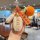 A hand holds a stylish key fob protector with a good luck tag and a knitted orange accessory, designed for the aima luna meta...