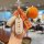 A hand holds a yadea m16/m11/m25h/c16 car key cover with a carbon fiber shell, featuring a crocheted orange tag and decorativ...