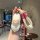 A hand holds a xiaomi su7 car key cover, featuring a card-style aluminum shell with a cute cartoon design and a white rope ke...
