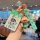A hand holds a vibrant exeed yaoguang car key cover featuring a cute cartoon character in colorful pajamas, paired with a mat...