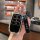 A hand holds a sleek black car key cover with silver accents, featuring a (pingan) charm and a circular emblem, designed f...