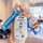 A hand holds a doraemon-themed wuling mini ev key cover, featuring a white case with colorful cartoon designs and a matching ...