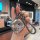 A hand holds a stylish wuling bingo car key cover featuring a cartoon design with chinese text, attached to a braided leather...