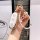 A hand holds a stylish ideal l8 key cover, featuring a white leather design with gold accents and decorative charms, perfect ...