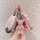 A hand holds a pink nissan qashqai key cover with a luxurious leather case, adorned with a sparkling teddy bear charm and a m...