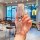 A hand holds a stylish pink toyota crown kluger key cover with a braided strap and decorative charms, set against a cozy café...