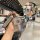 A hand holds a sleek, metallic renault key cover with a leather strap, showcasing its front view in a modern café setting. th...