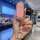 A hand holds a pink aito m9 key cover with a glittery texture and a sparkling ring keychain, set against a modern café backdr...