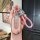 A hand holds a wuling hongguang mini ev key cover with a pastel pink, textured design and a braided pink strap, featuring a d...