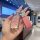 A hand holds a stylish pink peugeot 308 key cover with a ds badge, featuring a glittery finish and a decorative keychain, set...