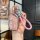 A hand holds a stylish roewe rx5 plus key cover with a pink glitter finish, featuring a braided pink strap and decorative cha...