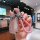 A hand holds a stylish car key fob with a pink braided leather strap and a silver charm, set against a modern interior backdr...