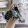 A hand holds a hyundai 4-button key cover with silver trim, featuring a cute bear charm and a stylish wrist strap, set agains...