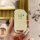 A hand holds a sleek, cream-colored kia 5-button key cover with a metallic edge, featuring a hold button and a small circular...