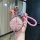 A hand holds a jetour dashing key cover for idm smart key, featuring a glittery pink design with a braided pink strap and dec...