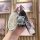 A hand holds a sleek, silver key cover for the 2024 hyundai sonata and ioniq 6, featuring a cute bear charm with blue eyes an...
