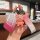 A hand holds a chery eq1 key cover with a gradient pink design, accompanied by a cute bear charm and a patterned strap, set a...