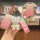 A hand holds a jaguar key cover with a gradient pink design, featuring a cute bear charm and a strap. the front view highligh...