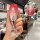 A hand holds a red hongqi h5 key cover with a gradient design and text, featuring a cat-ear keychain. the front view highl...