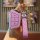 A hand holds a pink jac ic5 key cover for the jianghuai hanto ev, featuring a sleek design with a leather strap and a decorat...