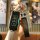 A hand holds a sleek, black baojun 510 key cover with a full-body remote protector design, featuring a leather strap and a de...