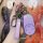 A hand holds a sleek purple nio s key cover with a matching leather strap, showcasing its modern design and functional button...
