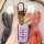 A hand holds a lufeng x2 smart key cover in soft pink with a sleek metal clasp, set against a vibrant kaws art backdrop.