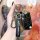 A hand holds a sleek, black ds-compatible aftermarket key cover for nissan, honda, and toyota, featuring a good luck strap an...