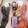 A hand holds a sleek, lavender suzuki jimny key cover with a metallic carabiner and logo, set against a vibrant, artistic bac...